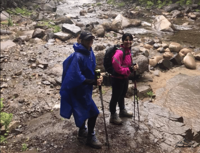 two hikers on a rocky trail in the rain wearing a rain jacket and a budget-friendly rain puncho