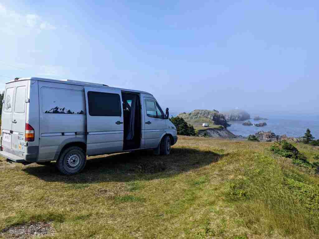 grey van parked by the ocean with a view on cliffs and rocky islands on a road trip in Newfoundland
