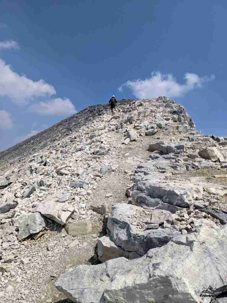hiker scrambling on the rocky trail nearing the summit on Mount Temple