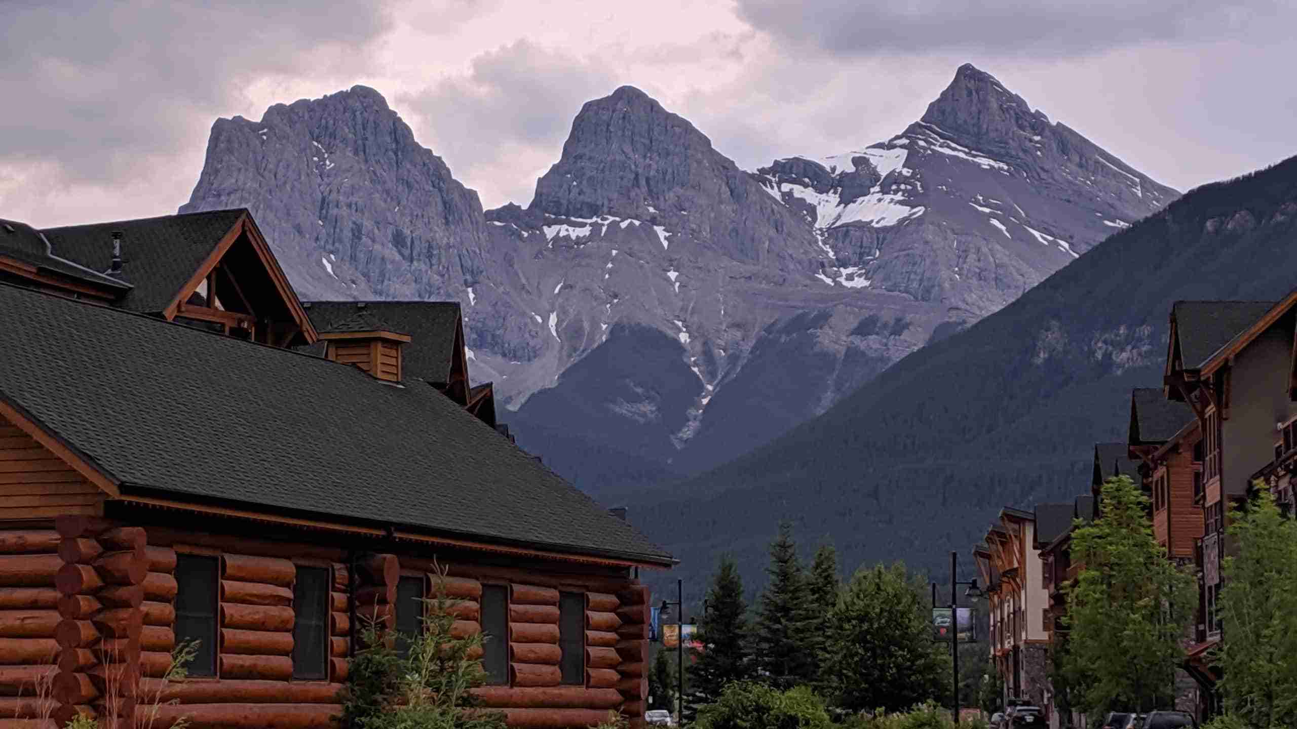 The three peaks of the Three Sisters behind a log cabin in Canmore