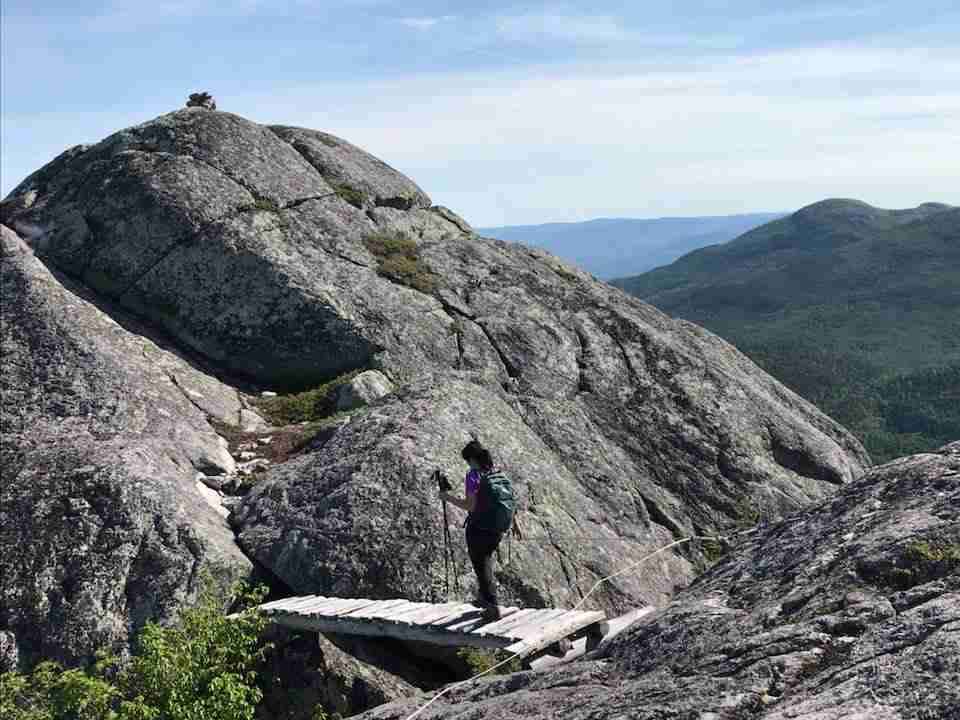 hiker on boardwalk traversing between two rocky hill on the summit of Mont des Morios