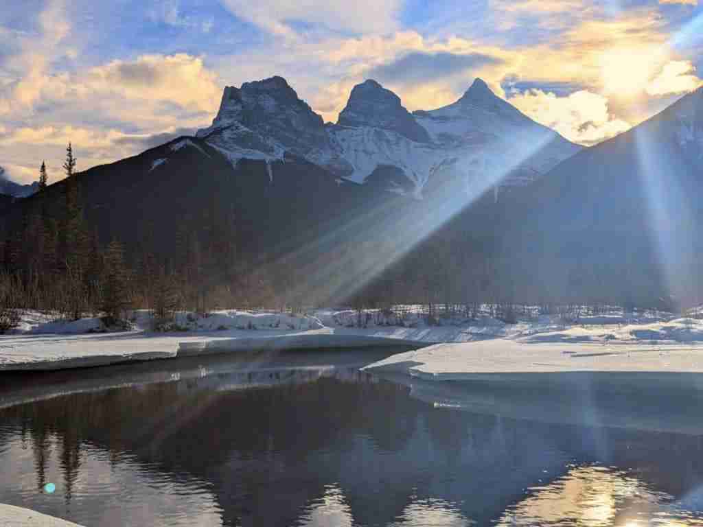 Le sommet enneigé de la montagne Three Sisters derrière un petit étang à moitié gelé à Canmore, en Alberta