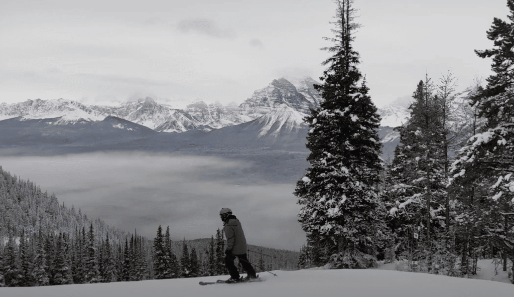 skieur skiant entre les arbres à Lake Louise Resort avec des montagnes enneigées au loin