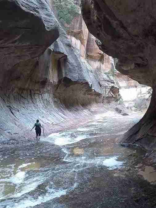 hiker walking in the Subway with a rockwall forming a tunnel and water flowing at the bottom
