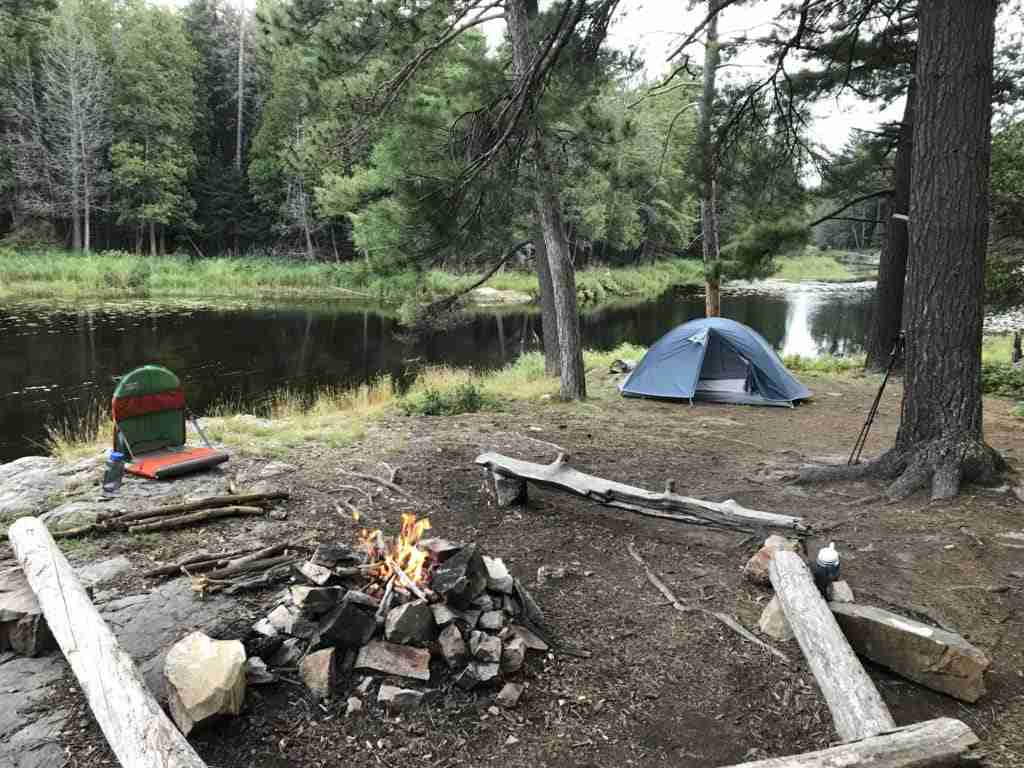 backcountry campsite with a tent, a campfire and a camping chair on the shore of a river