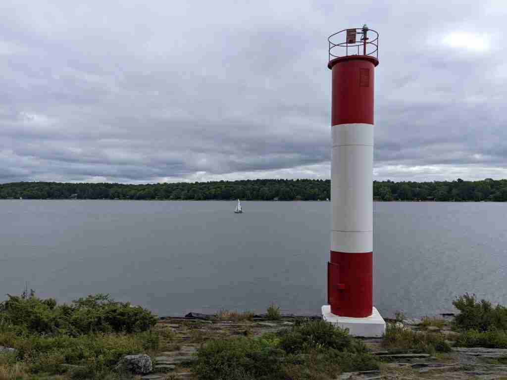 white and red striped lighthouse on Georgian Bay with a sailboat in the distance