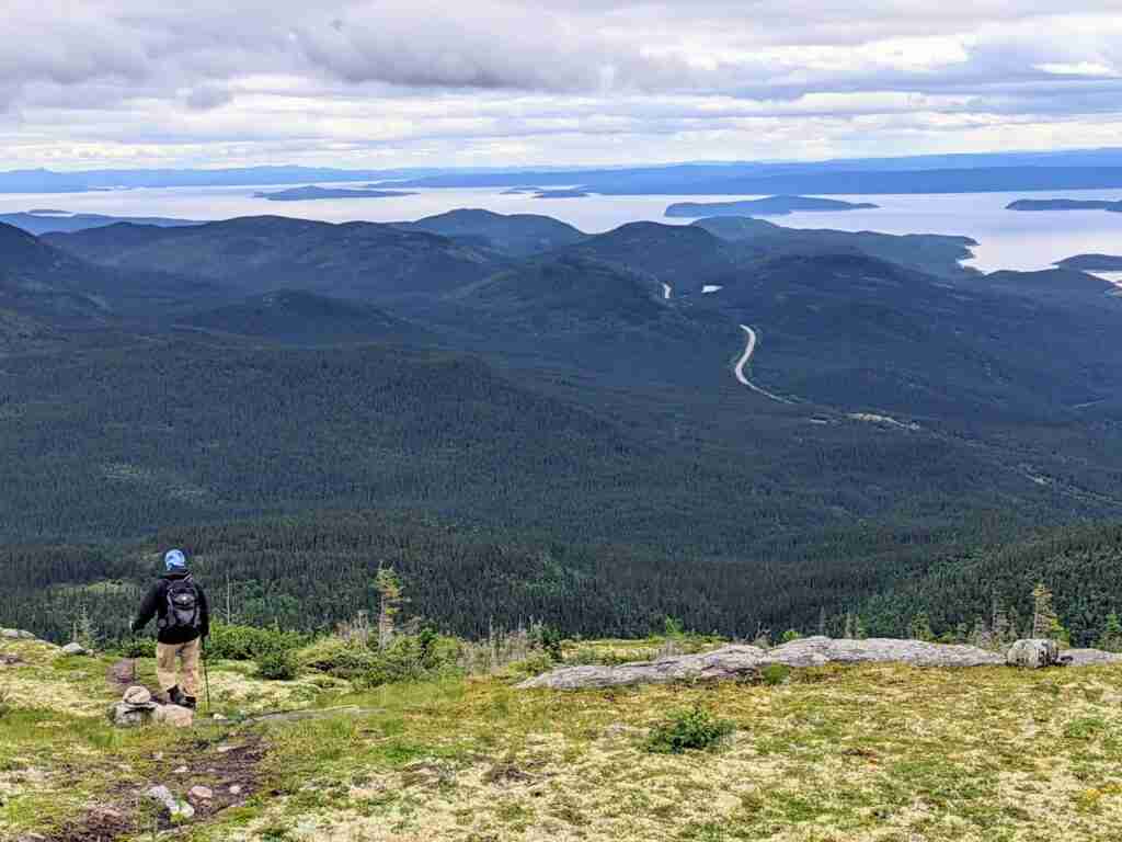 randonneur dans un pré alpin avec les collines des monts Groulx et le réservoir Manitougan au loin