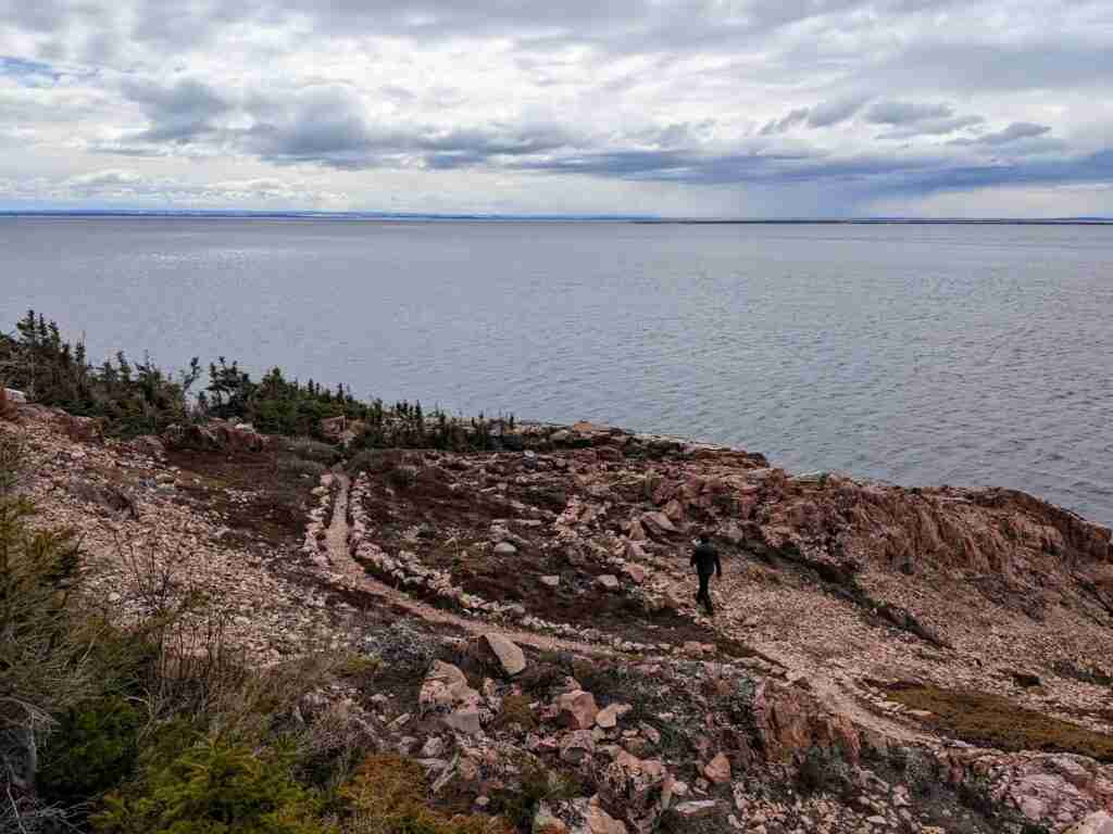 hiker walking on the red dirt trail along the St. Lawrence River in Tadoussac