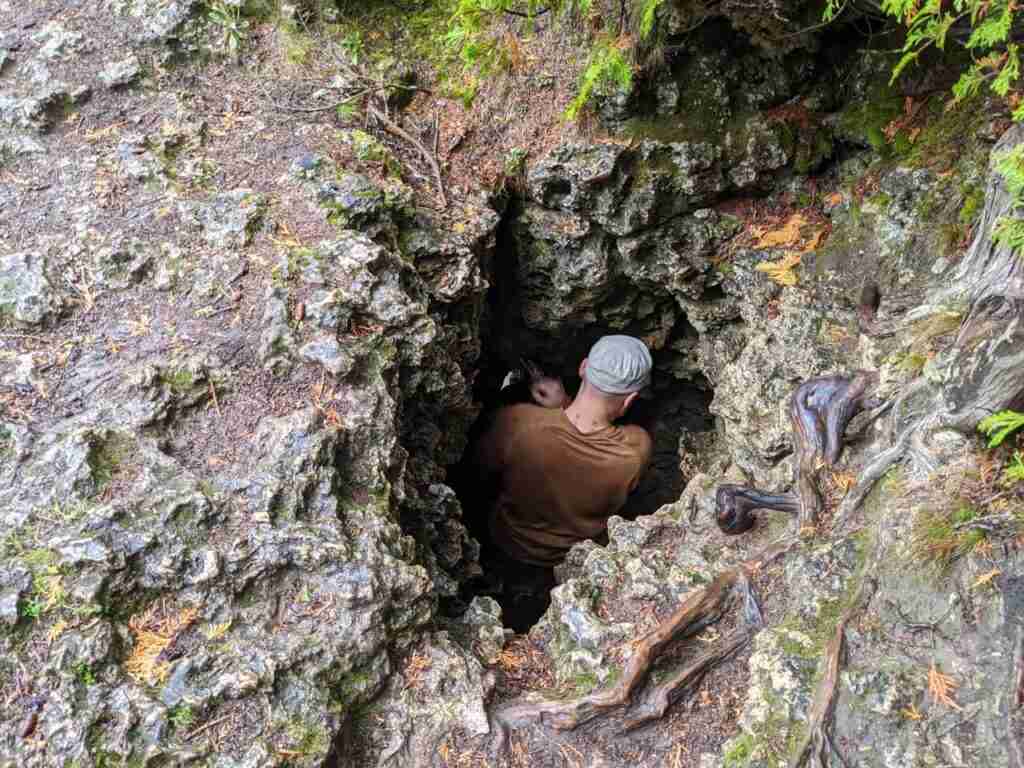 Hiker climbing down a hole in the ground to get beneath the overhang on the Bruce Trail in Bruce Peninsula National Park