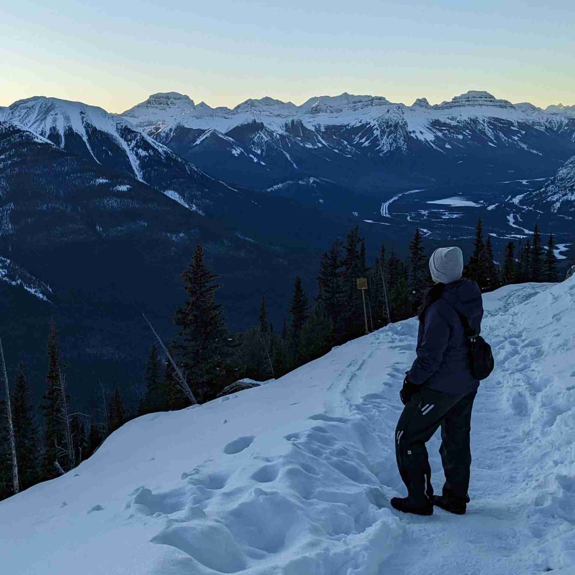 hiker standing on a snowy trail looking at the mountain range in the distance