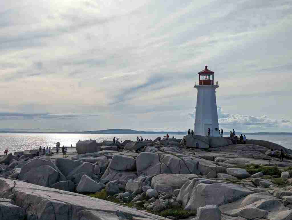 Nova Scotia's Peggy's Cove Lighthouse on the white sandstones, with many tourists wandering the grounds