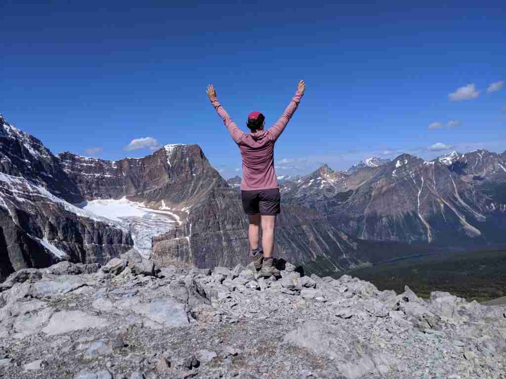 woman hiker standing alone on top of a mountain with arms outstretched in victory