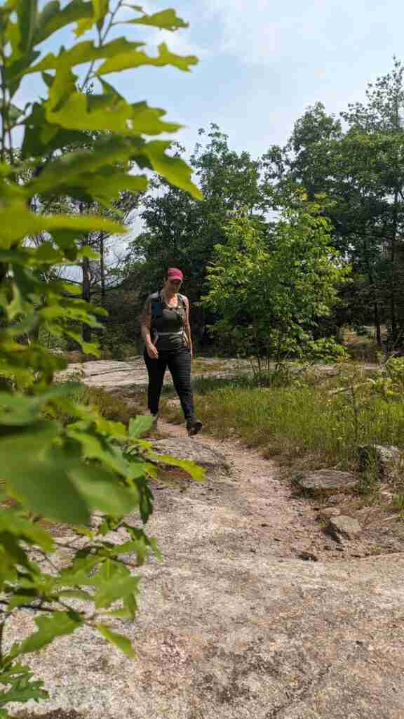 hiker on a dirt trail surrounded by trees wearing a tank top and black pants