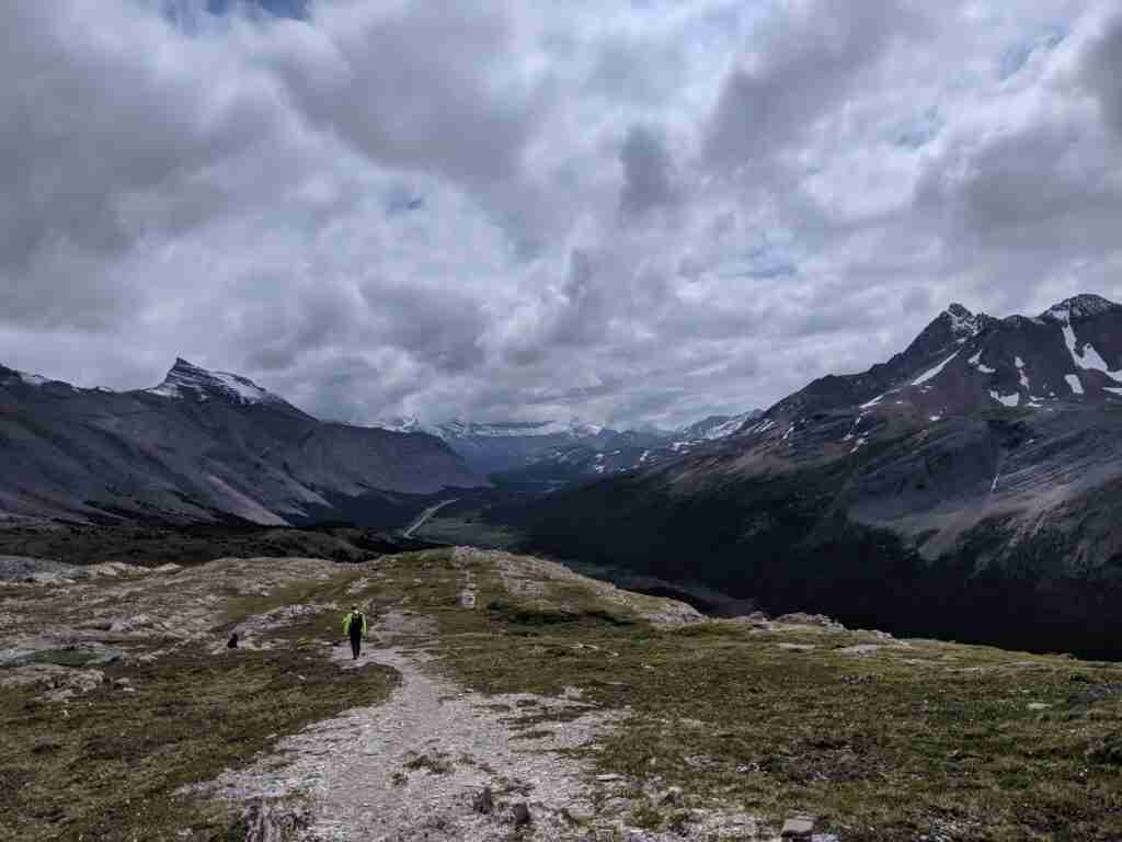 randonneur sur un sentier rocheux dans une prairie alpine avec les montagnes en toile de fond