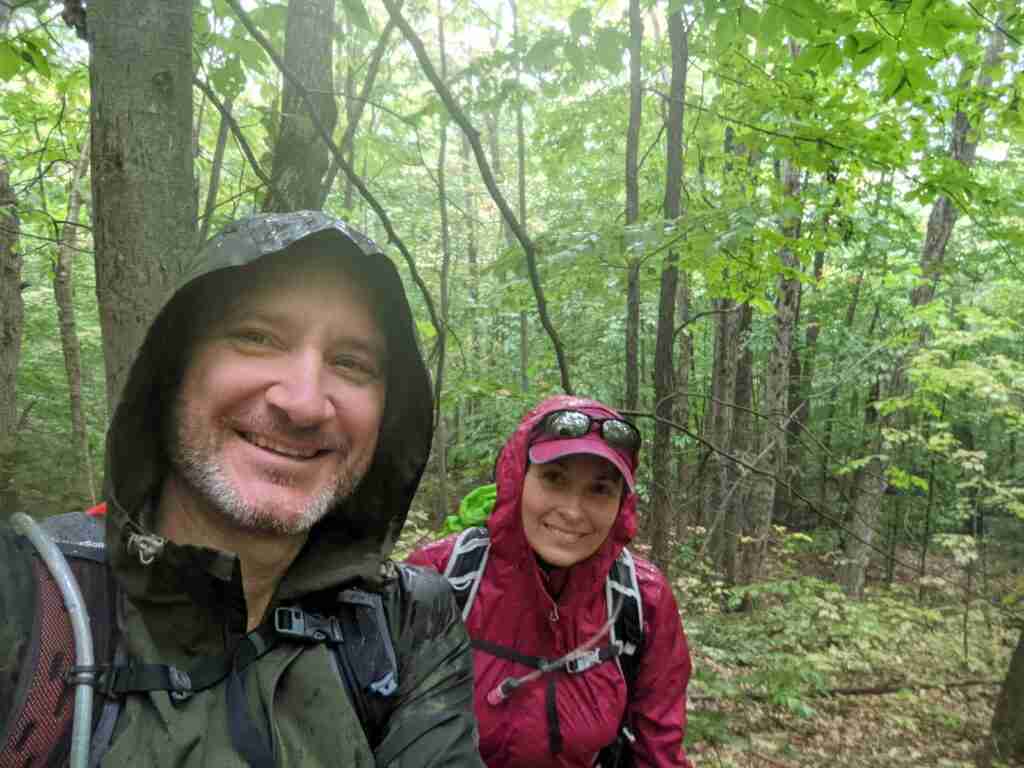 two hikers in a green rainy forest with their rain gear on
