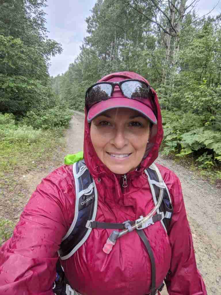 hiker in the rain on the trail bordered by trees wearing rain jacket