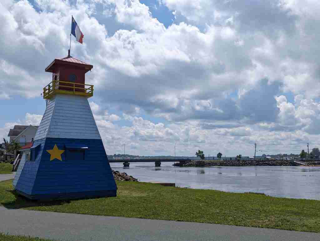 red white and blue lighthouse with the yellow star representing the acadian flag set by the water