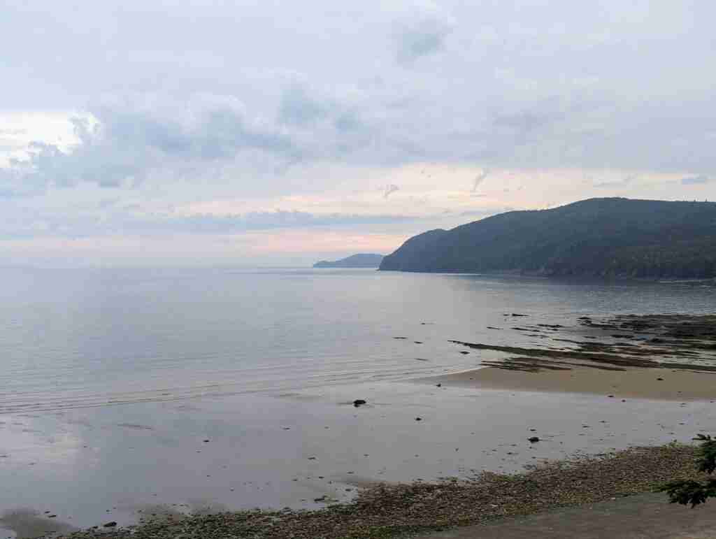 waves hitting the sandy beach with the green hills in the distance