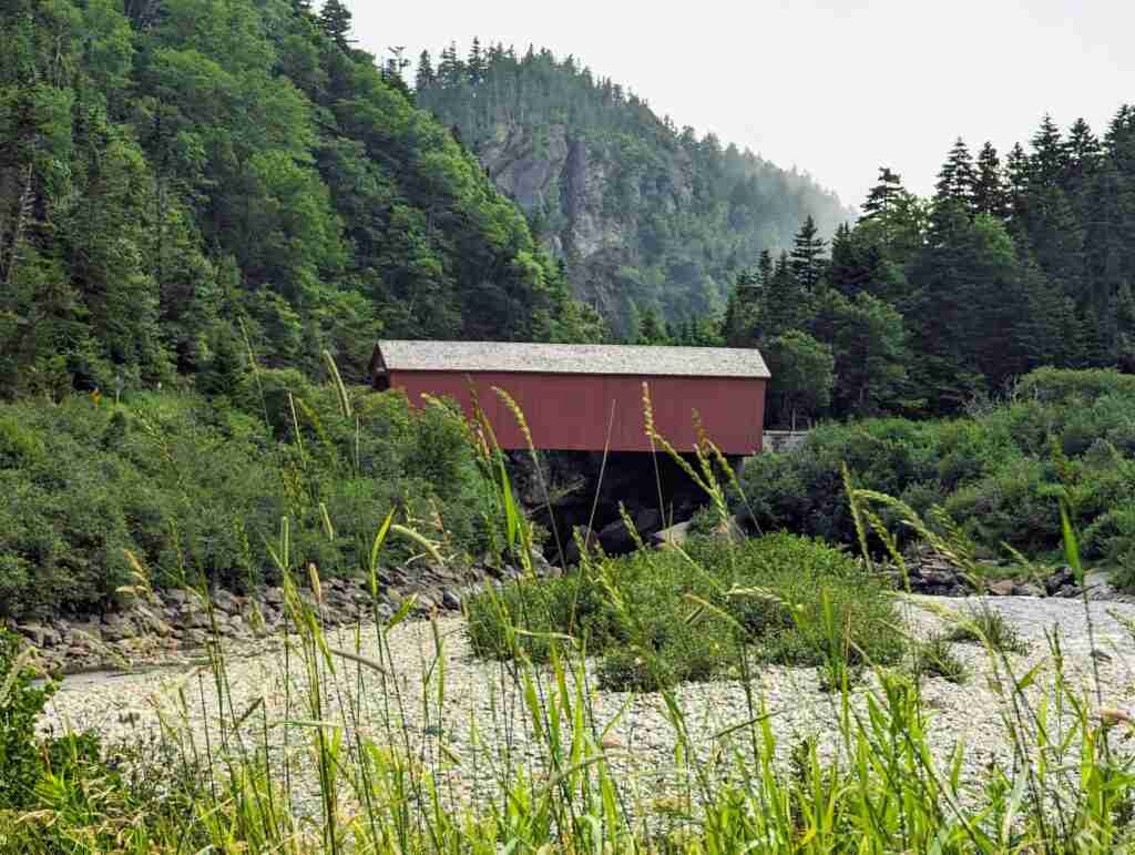Red covered bridge over the river with high forested hills on each side