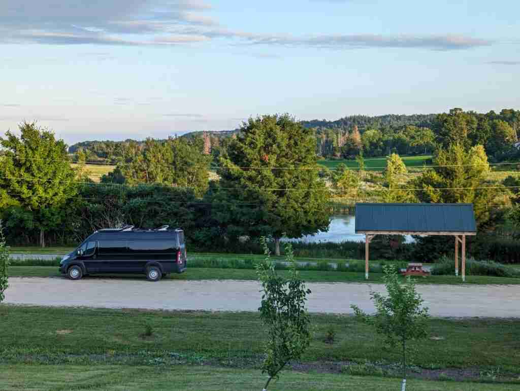 black camper van parked by a picnic table with a gazebo in a wooded area on a New Brunswick road trip