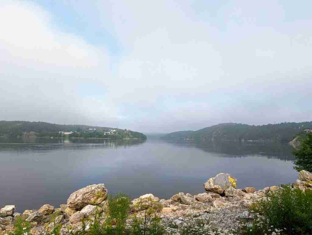 rocky shore of St John River with the green hills on the far shore