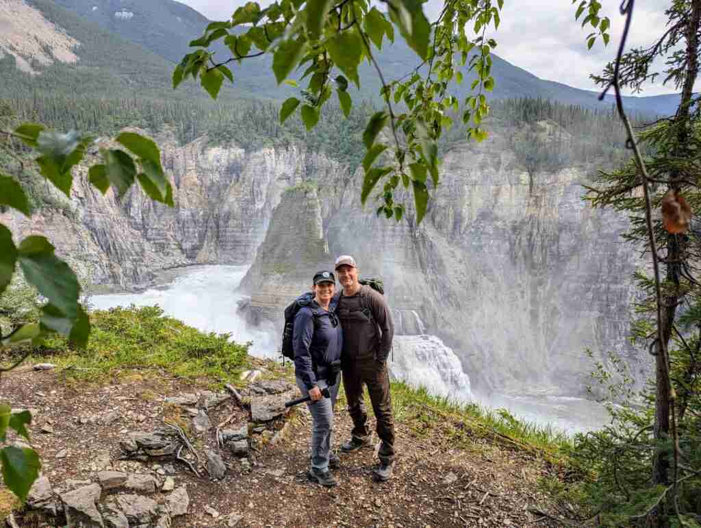 two hikers posing in front of the raging Virginia Falls during flightseeing tour of Nahanni National Park