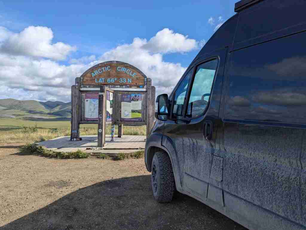 Black camper van parked in front of the Arctic Circle sign on the Dempster Highway