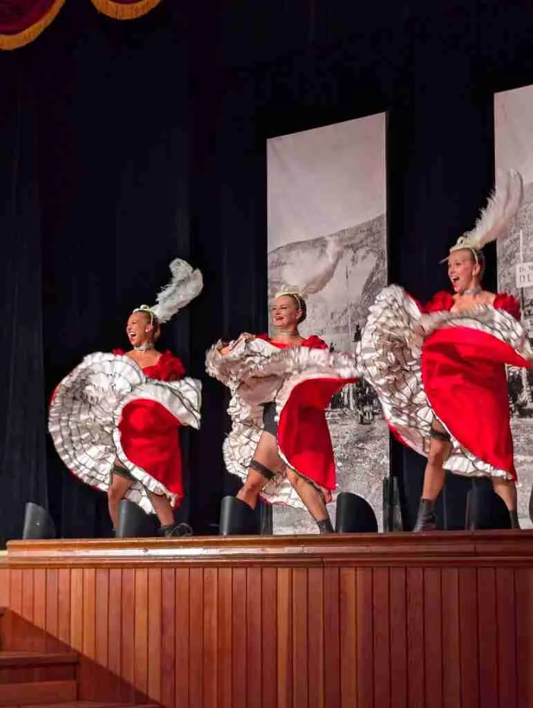 Trois femmes en robes rouges et chapeaux à plumes blanches dansent pendant un spectacle de cancan au Diamond Tooth Gertie's