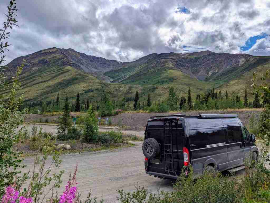 black camper van parked in parking area surrounded by mountains in Tombstone Territorial Park