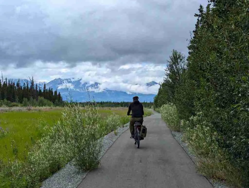Cycliste sur une piste cyclable pavée à Haines Junction avec les montagnes au loin
