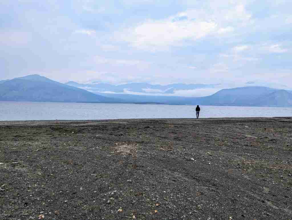 homme debout au bord de l'eau avec des montagnes sur la rive opposée, près de Destruction Bay, au Yukon
