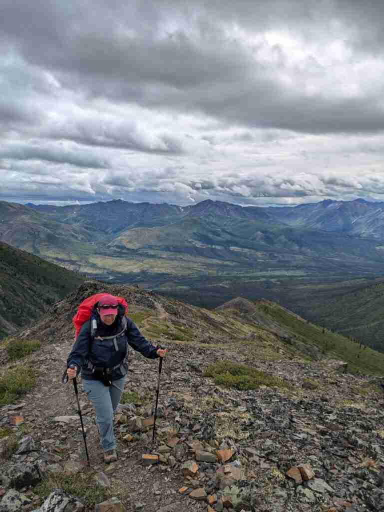 hiker wearing a rain jacket and a rain cover over her backpack on a mountain trail