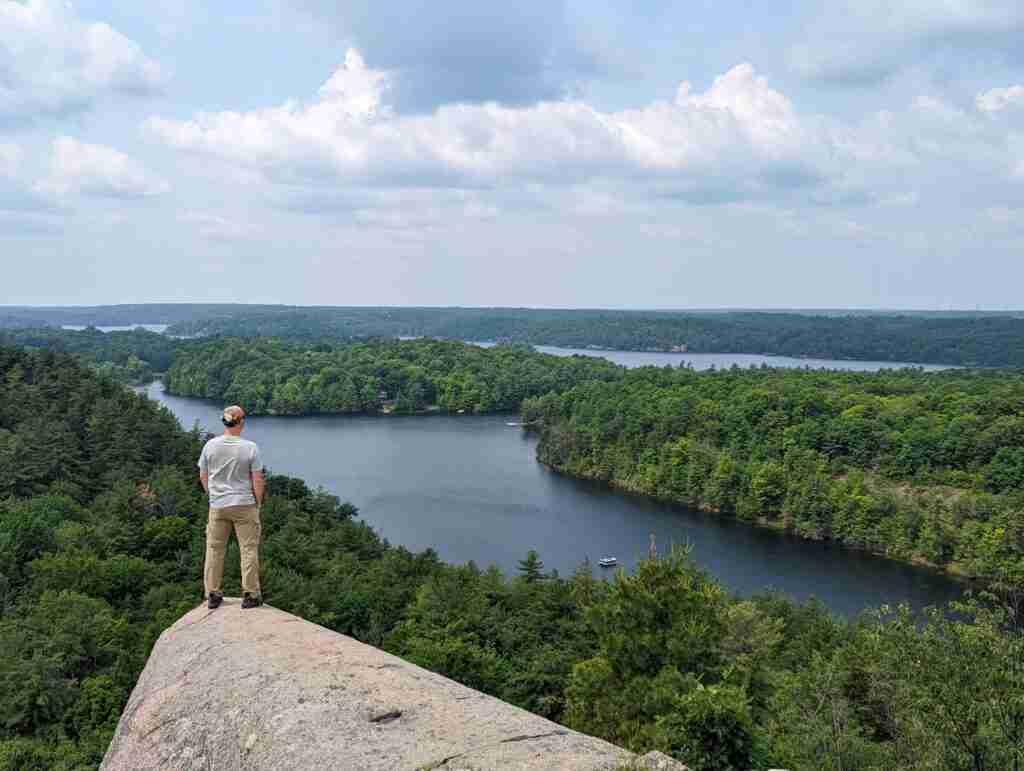 hiker standing on a rock cliff looking out at the lakes and green forests below