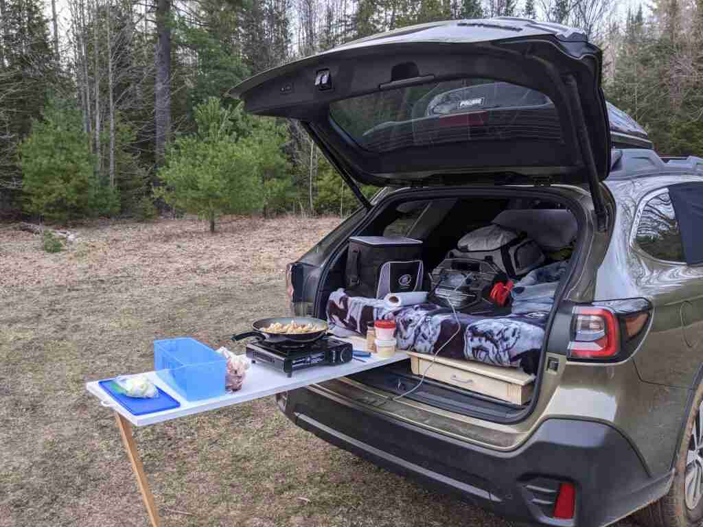car packed for a road trip with a makeshift kitchen and food cooking on a small camping stove