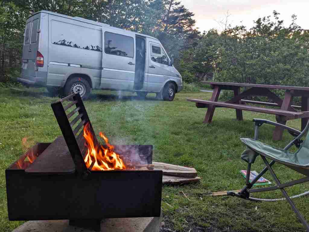 van parked on a campsite with a campfire burning