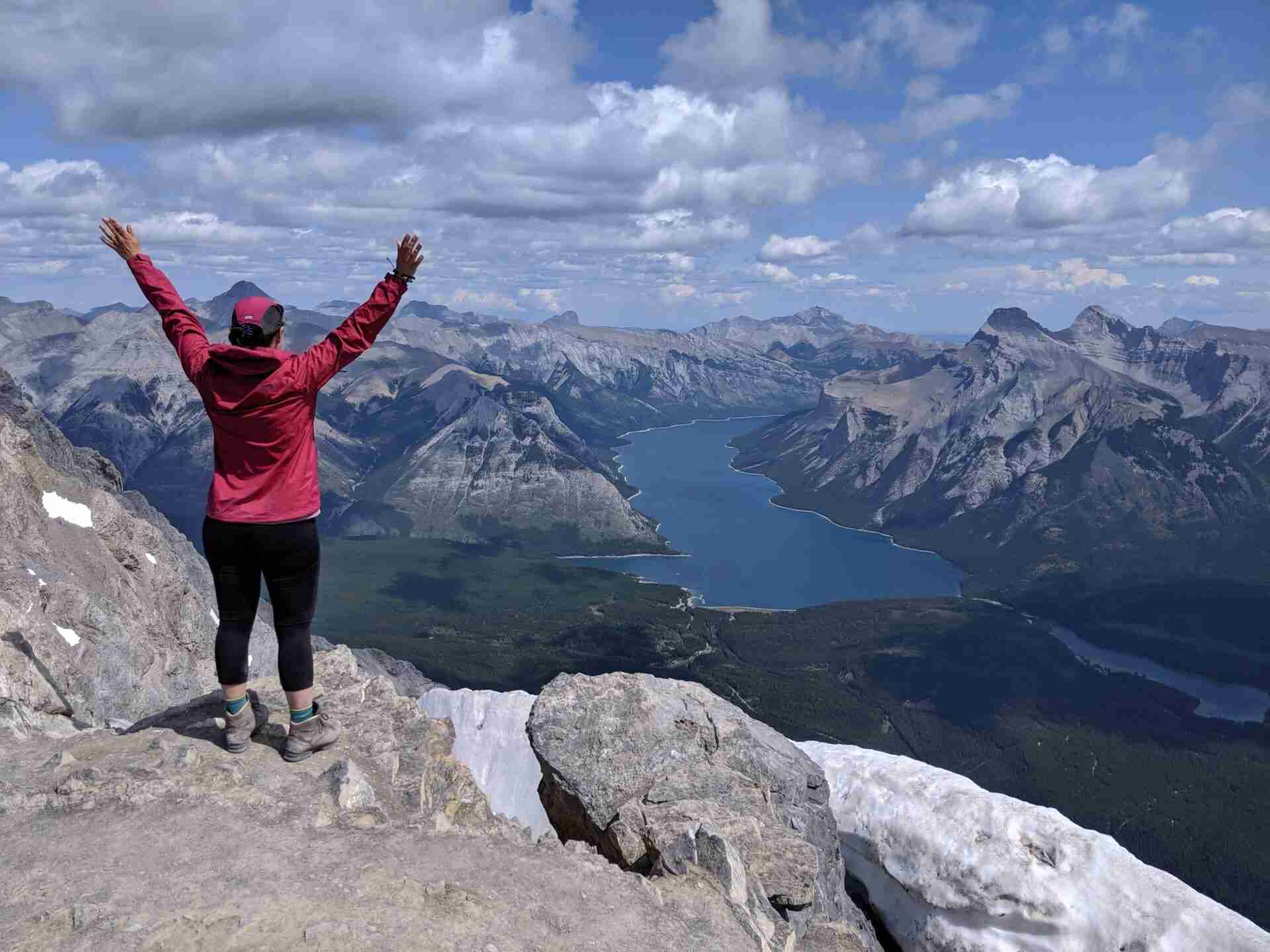 Adventuresome Jo standing on top of a mountain with her arms outstretched looking out at the vast mountain range